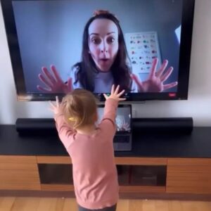 Child hands hands up to a screen where Mme Amy is visible and giving child a high five.