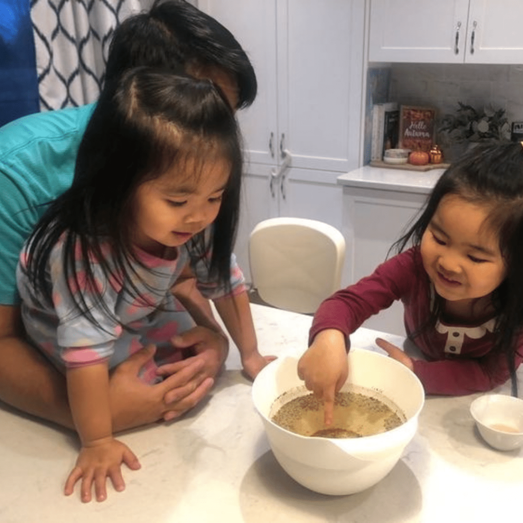 Children learning French while completing a science activity with their parent. Child is dipping her finger in a science experiment and smiling.