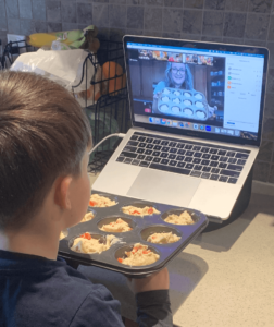 Child watching virtual French baking class with muffin tin in front of him