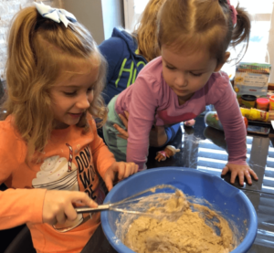 Two young girls stirring flour into a bowl and smiling.