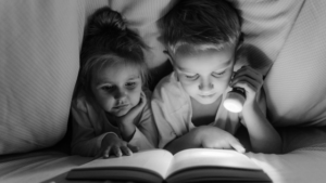 Two children are reading a children's French chapter book under a cover with a flashlight.