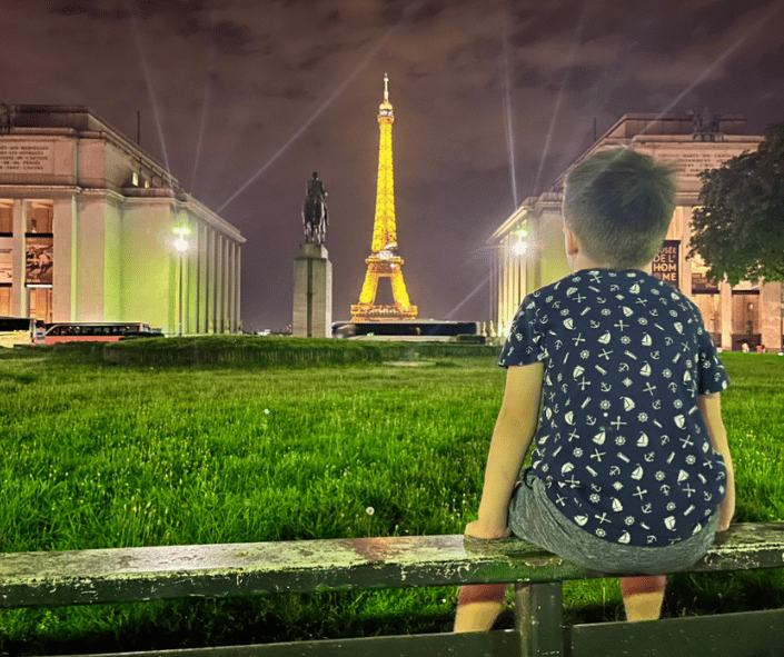 Boy sits watching the Eiffel Tower sparkle during a Family trip to Paris