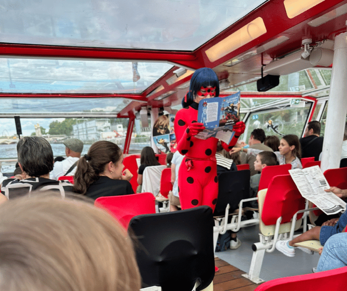 An image shows an actor dressed as Ladybug from Miraculous TV show, acting out her role on a boat cruise in Paris, France.